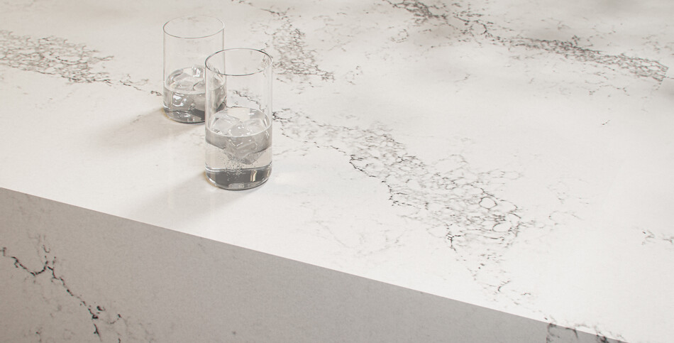 Two glasses of water sit on a countertop of dove white Statuario Maximus quartz with broad light-gray veins.