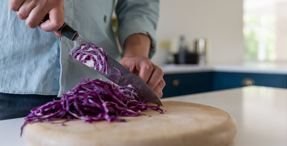 A man cuts red cabbage on a cutting board, which sits on a kitchen island of Empira White quartz.