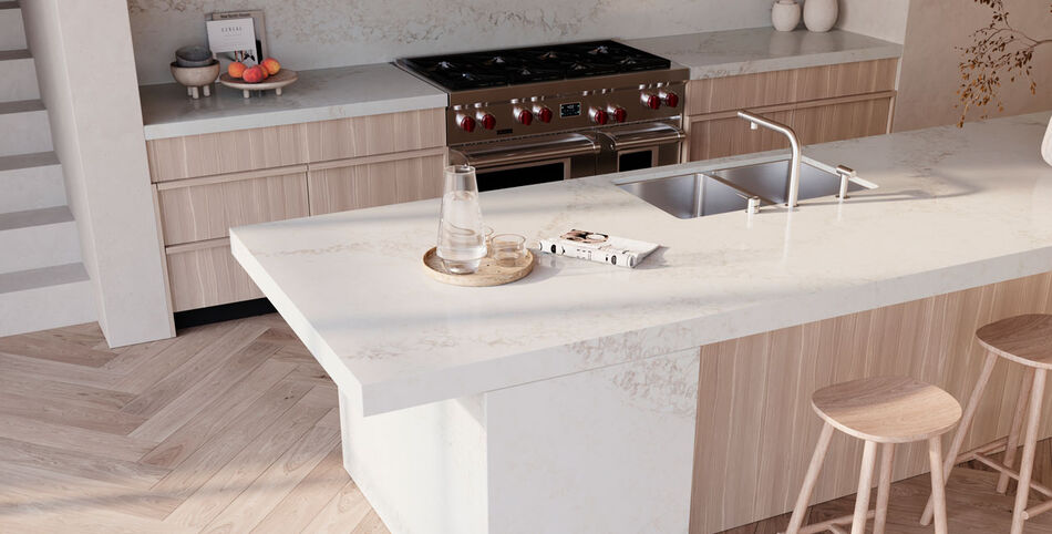 Modern kitchen island with a white veined Calacatta Lacebound Caesarstone ICON countertop, light wood cabinets, stainless steel sink and faucet, and herringbone wood floor.