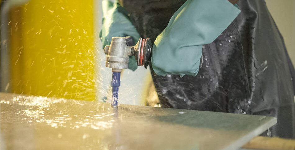 Hands in protective gloves using a power tool to cut or grind a metal surface.